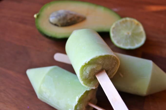 Popsicles on a wooden table, next to avocado and lime.