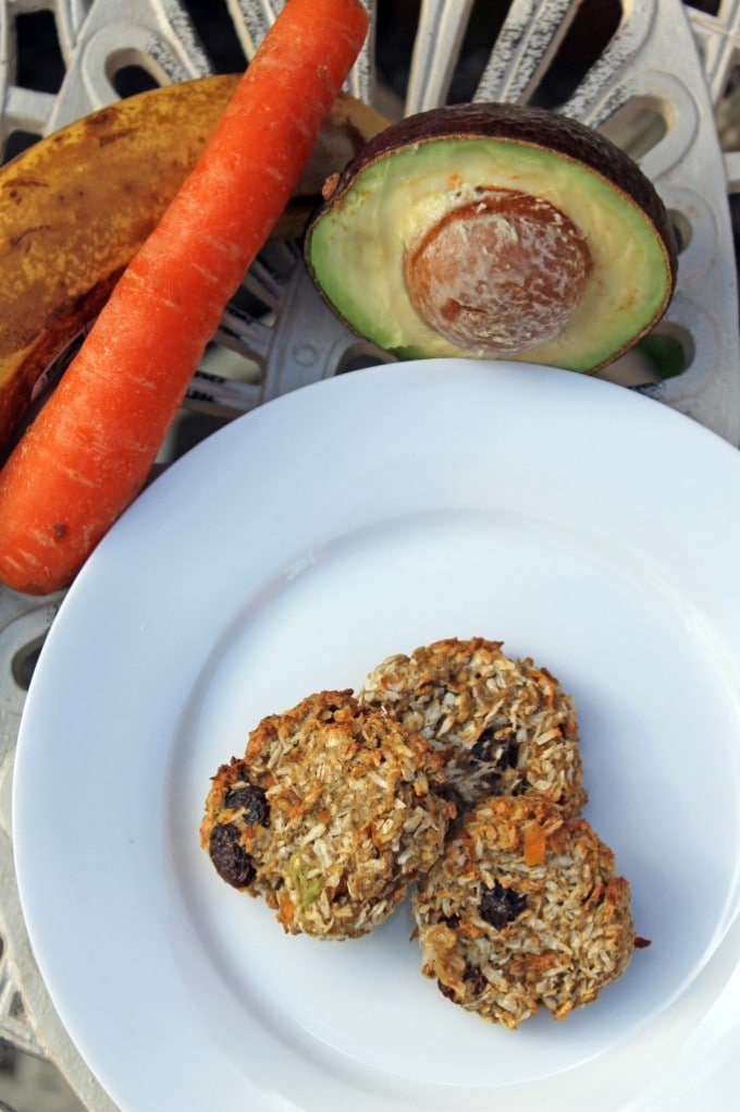 A plate of cookies next to an avocado and a carrot.