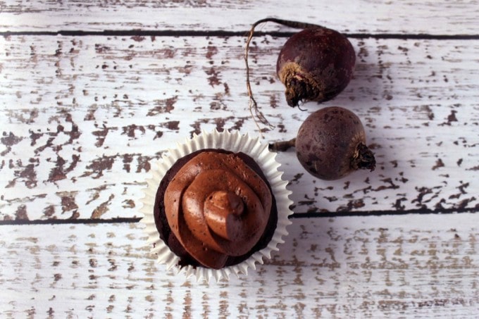 Frosted cupcake on a table next to two beets.