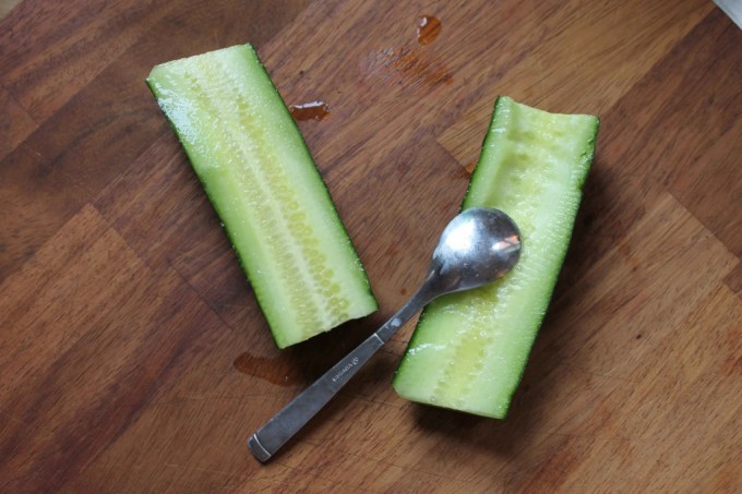 A spoon removing the middle of a cucumber.