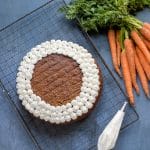 Overhead of easy carrot cake with maple whipped cream piped in dots around the edge. Next to a bunch of carrots.