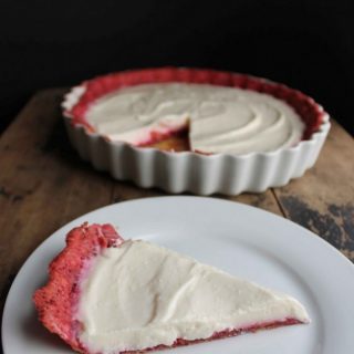 A slice of pie on a plate in front of the rest of the pie.