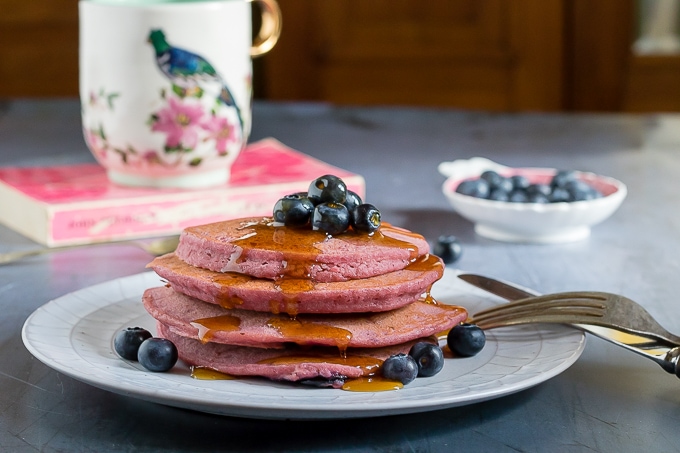 A stack of bright pink gluten free buckwheat pancakes made with pureed beets and topped with blueberries. 