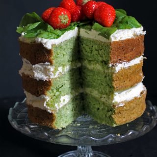 Spinach Coconut Yogurt Cake with a slice cut out showing the green cake. Topped with strawberries.