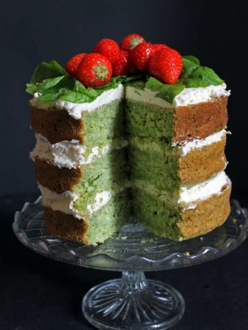 Spinach Coconut Yogurt Cake with a slice cut out showing the green cake. Topped with strawberries.