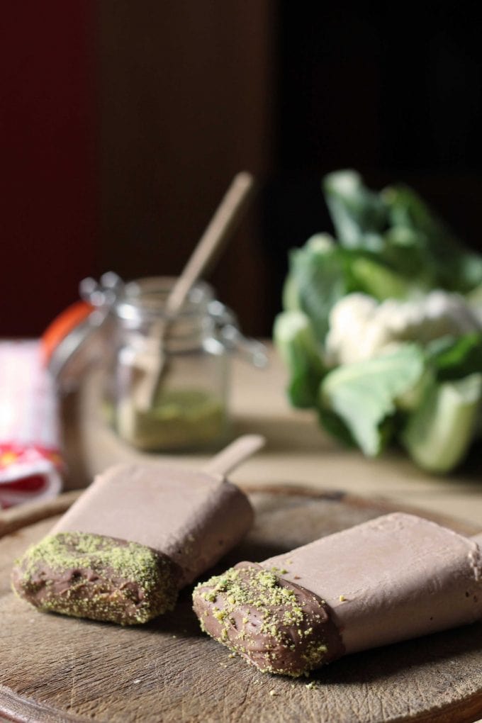 Chocolate Cauliflower Popsicles on a wooden board in front of a head of cauliflower.