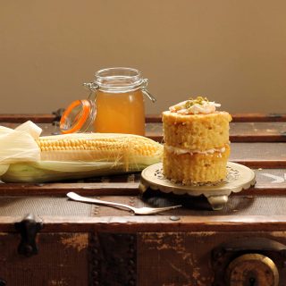 A mini layer cake next to a cob of corn.