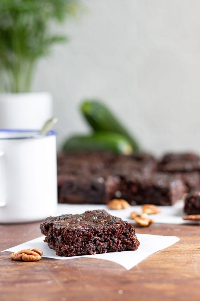 Side view of a courgette brownie on baking paper in front of a mug of coffee