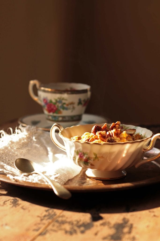 A tray on a table, with oatmeal in a bowl and a vintage cup of tea.