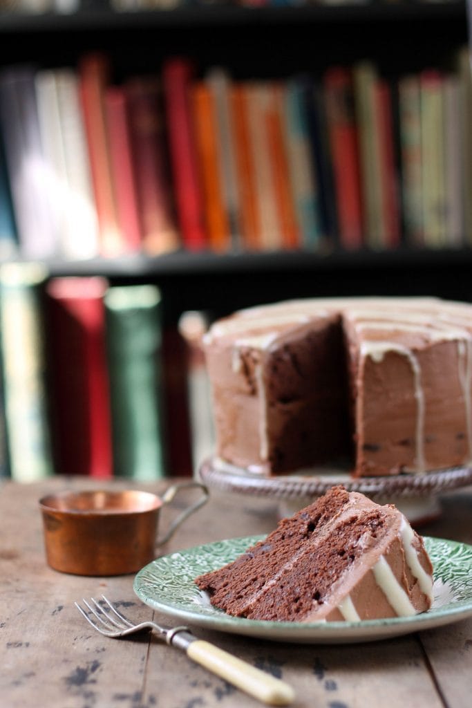 A piece of cake on a plate with the cake behind it.