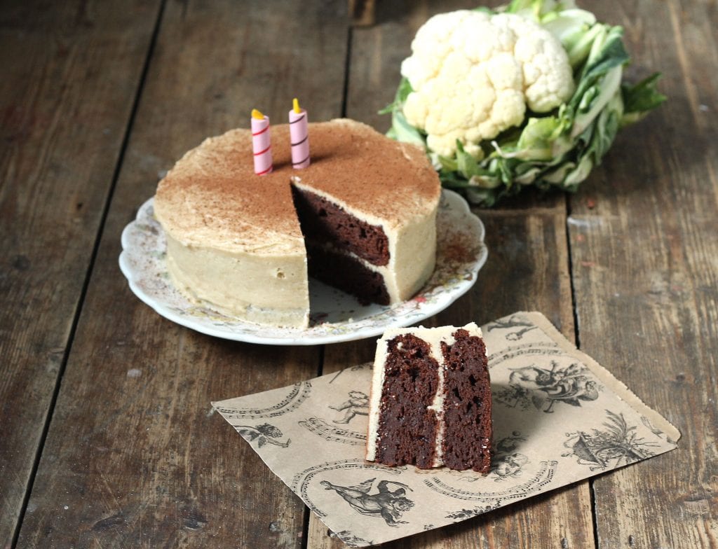 Slice of cake in front of cake, with cauliflower in the background.