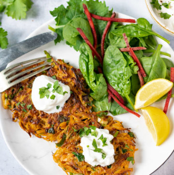 A plate with Moroccan Carrot Fritters, with sour cream, salad and wedges of lemon