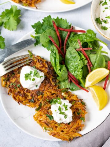 A plate with Moroccan Carrot Fritters, with sour cream, salad and wedges of lemon