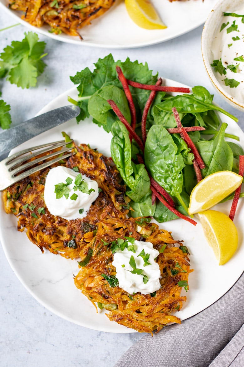 A plate with Moroccan Carrot Fritters, with sour cream, salad and wedges of lemon