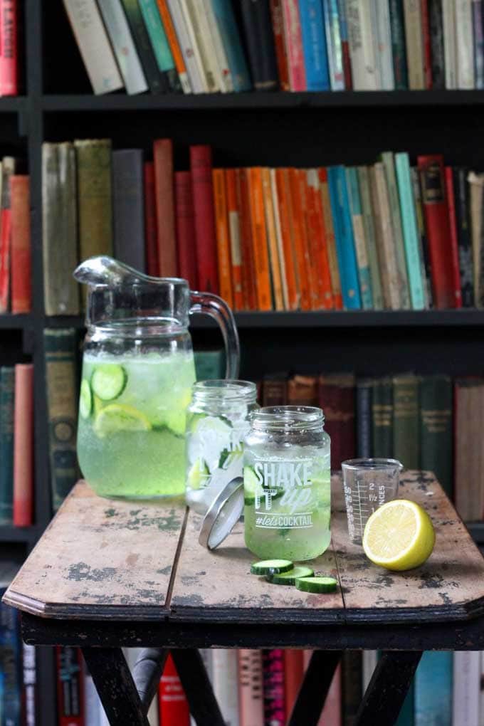 A table with drinks and a jug, in front of bookshelves.