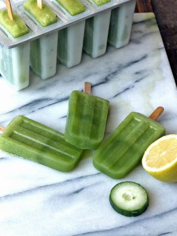 A marble board with three cucumber popsicles on it.
