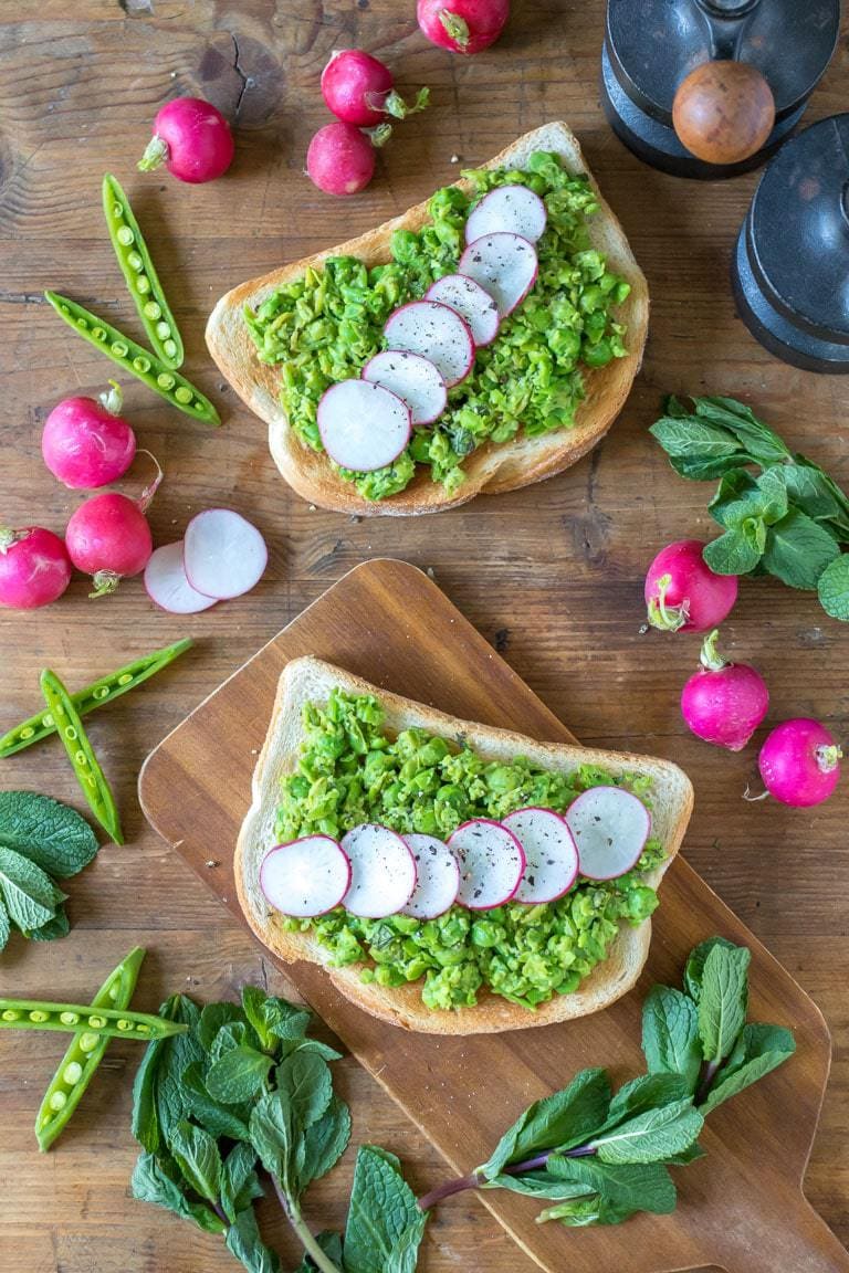 Slices of toast covered in peas and radishes on a wooden table.