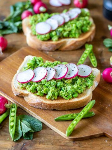 A sandwich sitting on top of a wooden cutting board, with Pea and Radish.