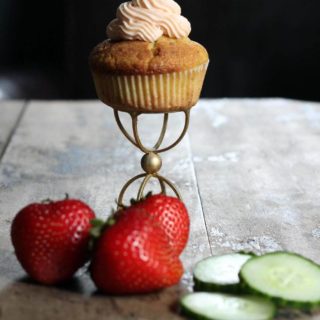 Cucumber cupcakes with pimms frosting on a gold stand next to strawberries and cupcakes