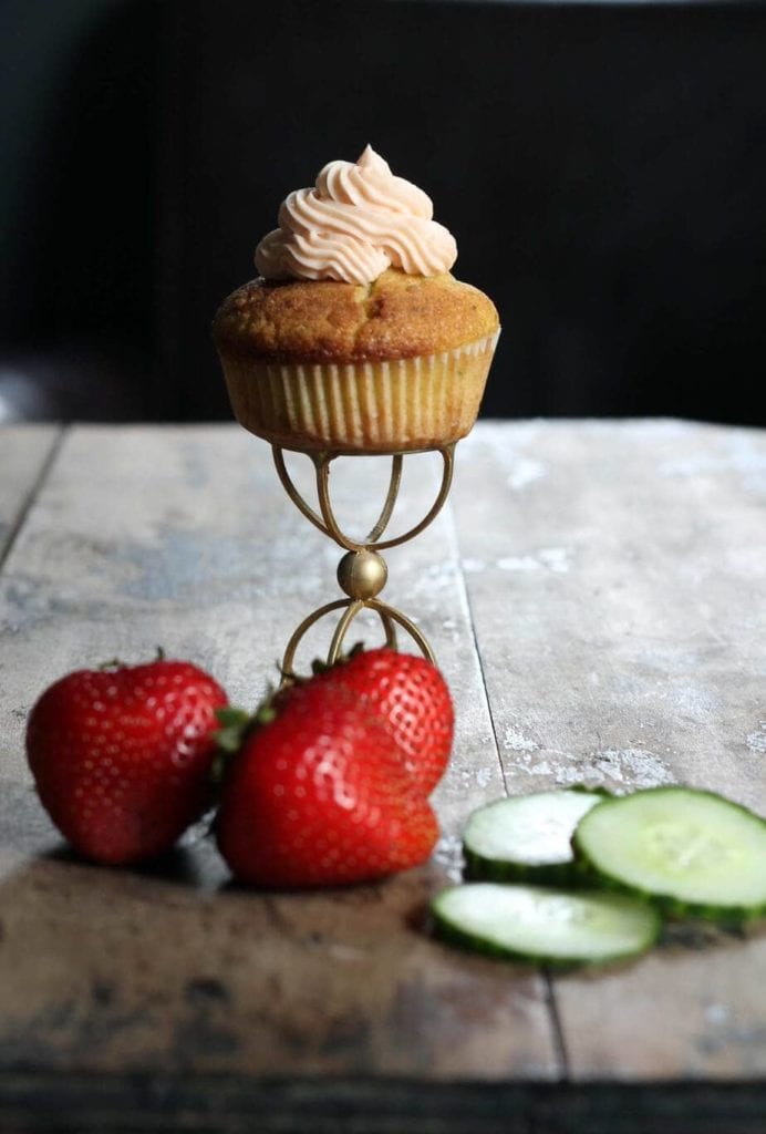 Cucumber cupcakes with pimms frosting on a gold stand next to strawberries and cupcakes