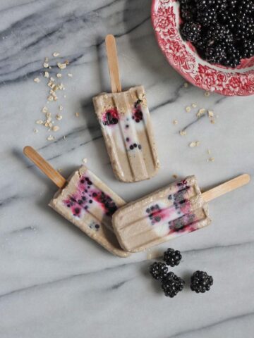 A marble board with three popsicles and a bowl of blackberries.