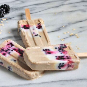 Three blackberry oat breakfast popsicles on a marble board.