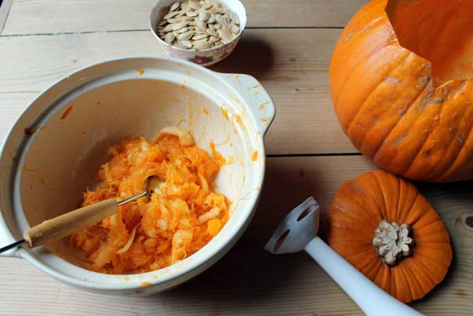 A table with a pumpkin and a bowl of pumpkin innards.