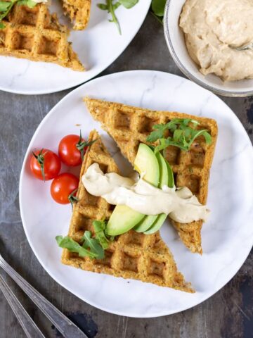 A table with plates of waffled falafels topped with avocado and hummus.