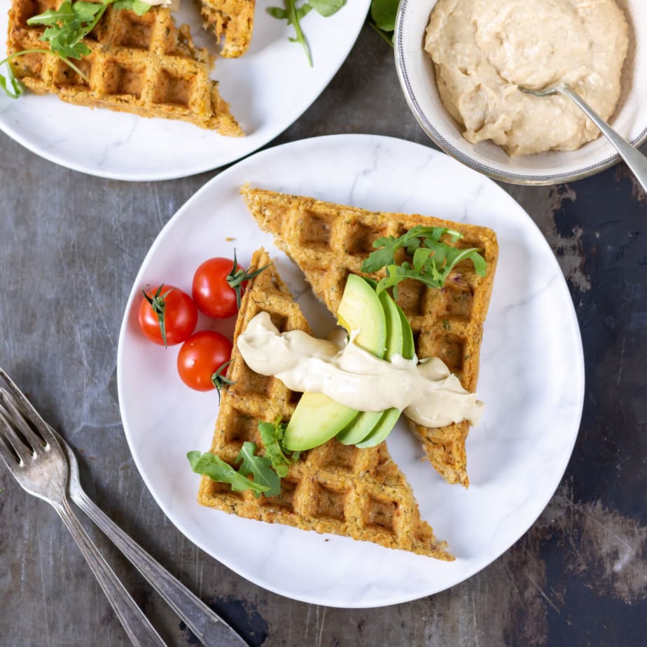 A table with plates of waffled falafels topped with avocado and hummus.