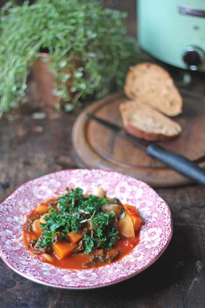 Stew in a bowl on a table, next to bread sliced on a cutting board.