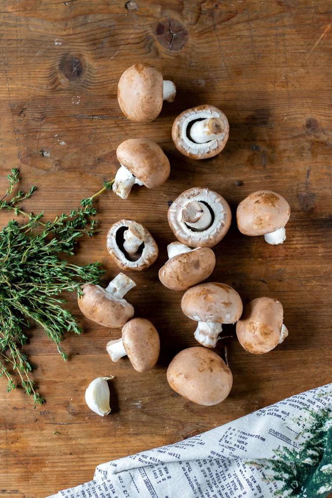 Ingredients for mushrooms on toast recipe for vegetarian or vegan breakfast, brunch, lunch or a light dinner. Mushrooms on a wooden table with garlic and sprigs of thyme.