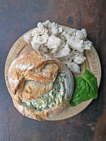 A round bread, hollowed out and filled with artichoke dip.