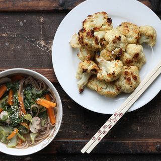 A table with a plate of roasted cauliflower and a bowl of noodle soup.