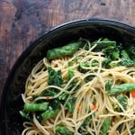 A bowl of spaghetti with asparagus, chilli and lemon on a wooden table.