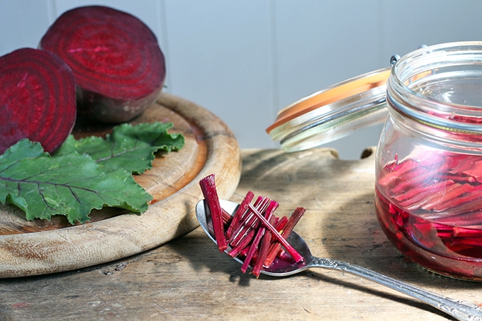A jar of quick Pickled Rosemary Beet Stems with a teaspoon of pickled beet stems in front