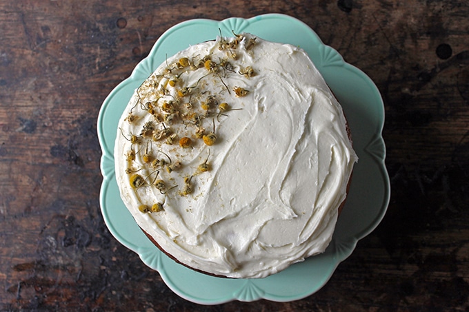 Chamomile Cake decorated on half the top with chamomile tea buds. Shown on a vintage cake stand.