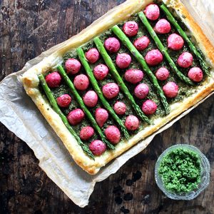 A tart with radishes and asparagus on a wooden table.