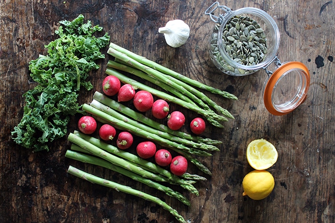 A table with radishes, asparagus, kale, lemon and pumpkin seeds.