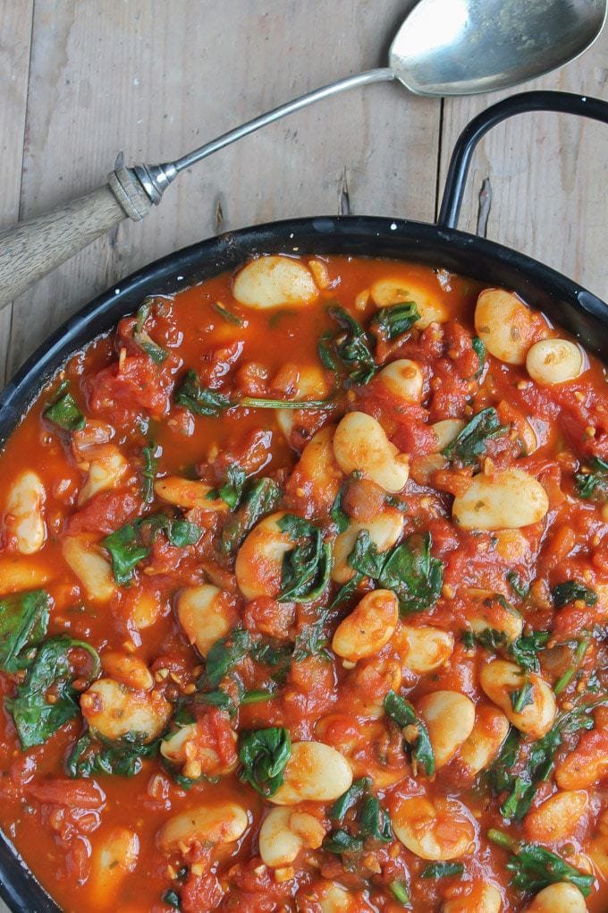 Close up of a dish of Spanish white beans in tomatoes with spinach.
