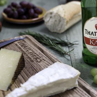 A bottle of cider and a wooden tray with cheeses.