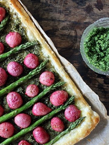 A tart with radishes and asparagus on a wooden table.
