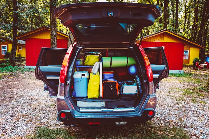 A car parked in front of a house packed with camping gear.