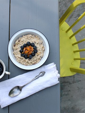 An outdoor table with a bowl of porridge topped with blueberries.
