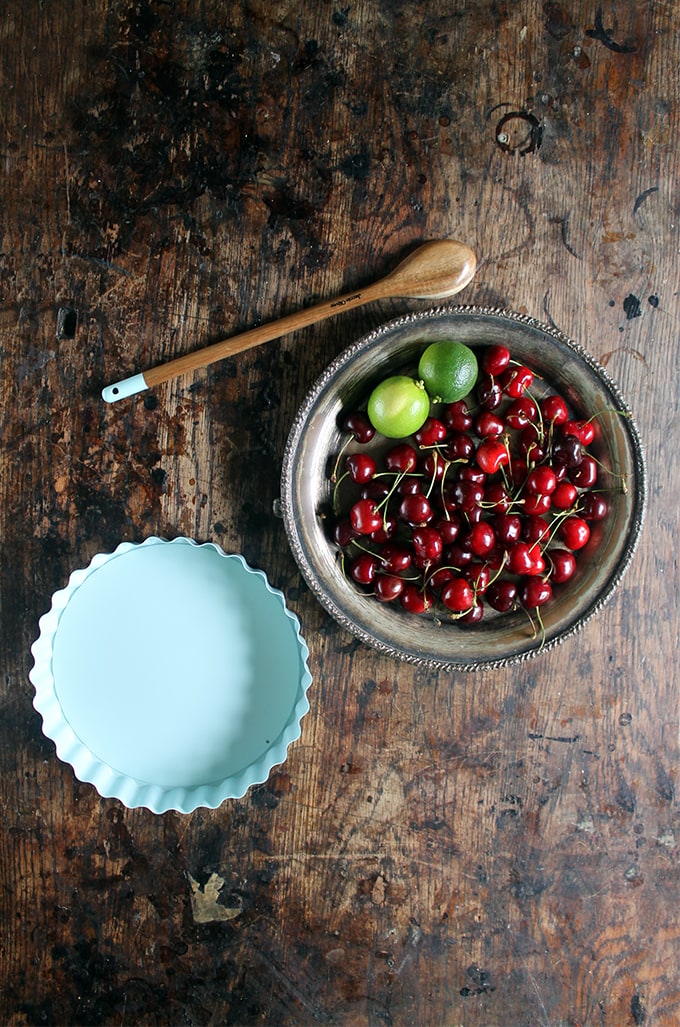 Fresh cherries and limes on a plate next to a pie pan.