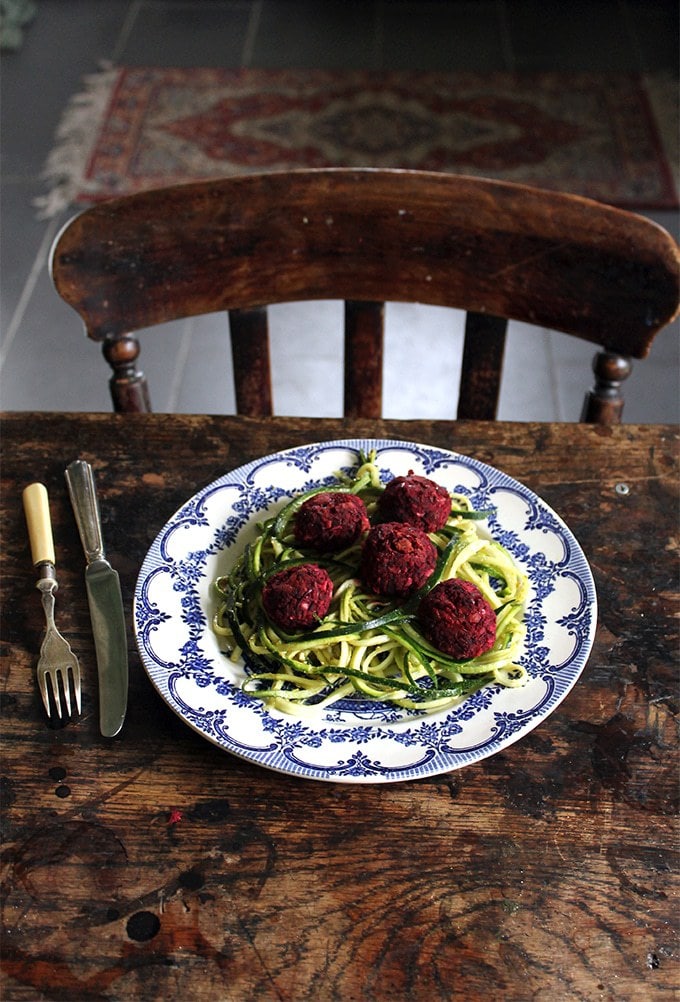 Table with a plate of zucchini noodles and meatballs made from beetroot.