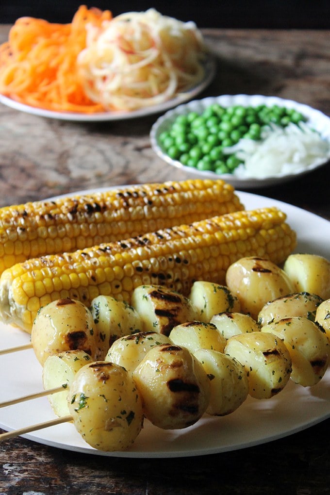 Close up of grilled corn and potatoes with peas, carrot and apple in the background - all for a Brazilian potato salad
