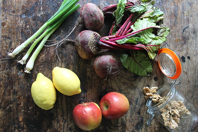 Flat lay of ingredients for Beetroot Salad: scallions, beets, lemon, apples, walnuts.