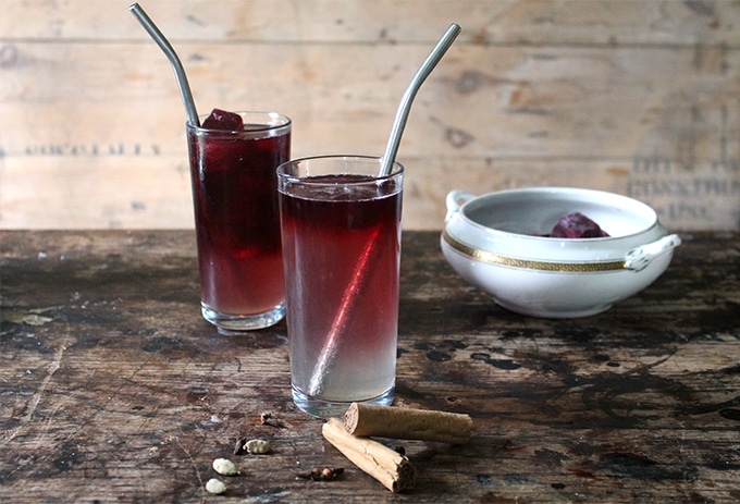 Two tall glasses with Mulled Gin Cocktail with Mulled Wine Ice Cubes and metal straws.
