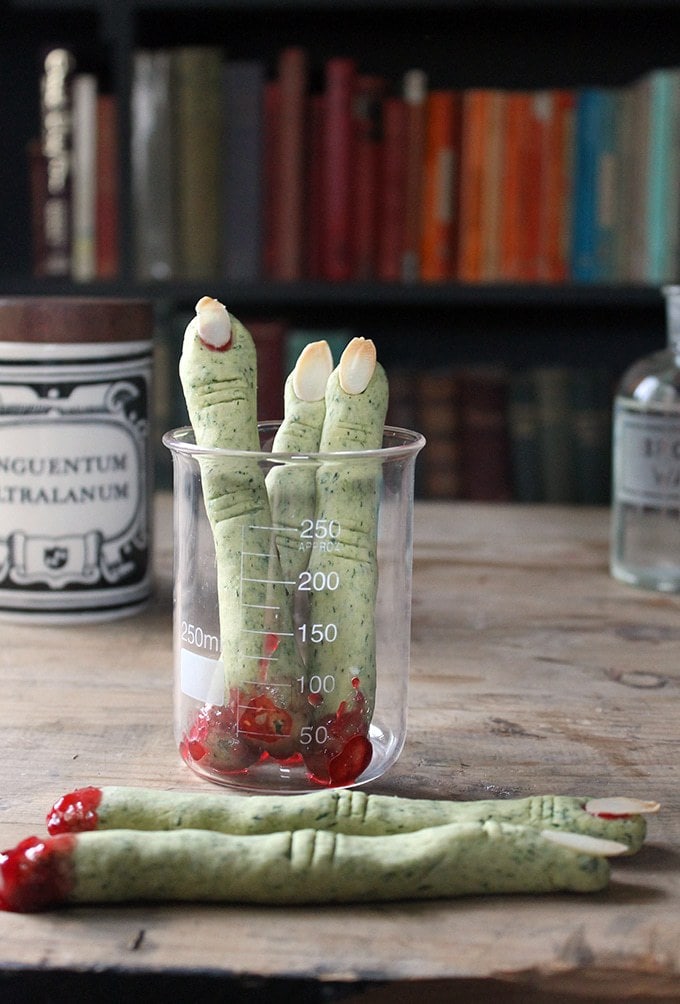 A science beaker filled with green cookies shaped like fingers.