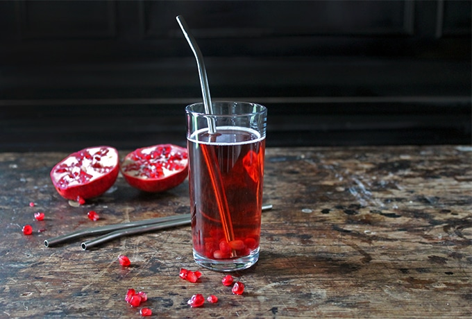 A glass of cocktail sitting on top of a table next to pomegranates.